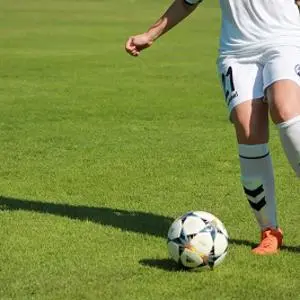 Lower body of a footballer in a white kit dribbling a ball across a green pitch.