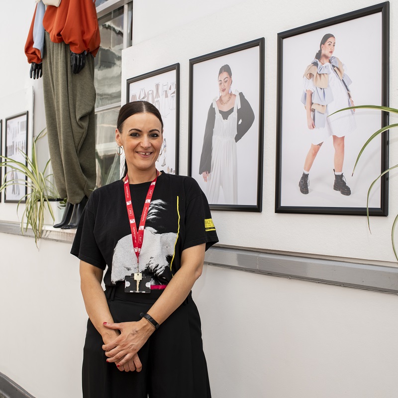 Student standing in front of their designs in the Fashion exhibit at the Art and Design Showcase