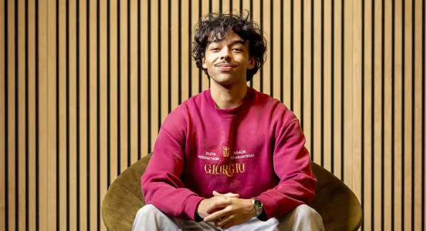 A young male student wearing a red sweater is posing confidently sitting in a chair