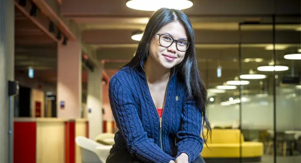 A young female student wearing glasses is smiling and in a relaxed posed in an open office space