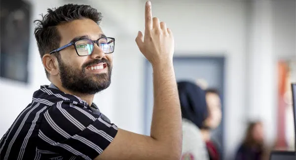 A male student wearing glasses a dark striped shirt is smiling in the classroom
