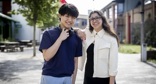 A young male and a female student and standing casually together on Leek Road campus smiling