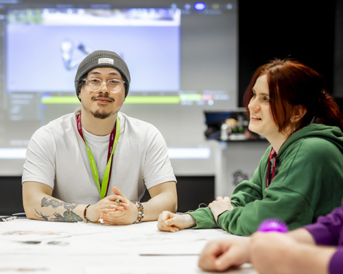 A group of casually dressed students are sitting at a table together, collaborating on games art work