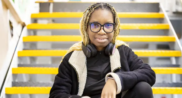 A casually dressed female student with glasses and braids is sitting relaxed on the stairs in the Science Centre