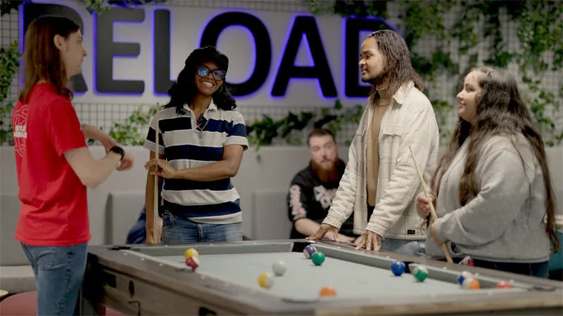A group of young diverse students are playing pool in the break out area