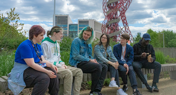 A group of young students who are dressed casually are socialising outdoors near the West Ham area