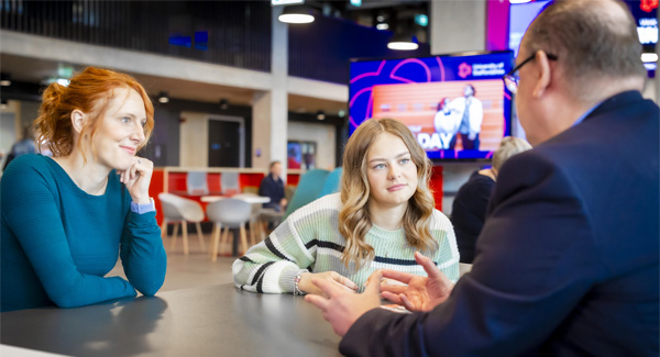 A female parent and student are sitting down chatting to a staff member at an open day inside a modern building