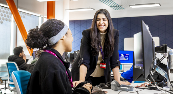 A female lecturer is chatting with a student in the computer lab, they are both smiling
