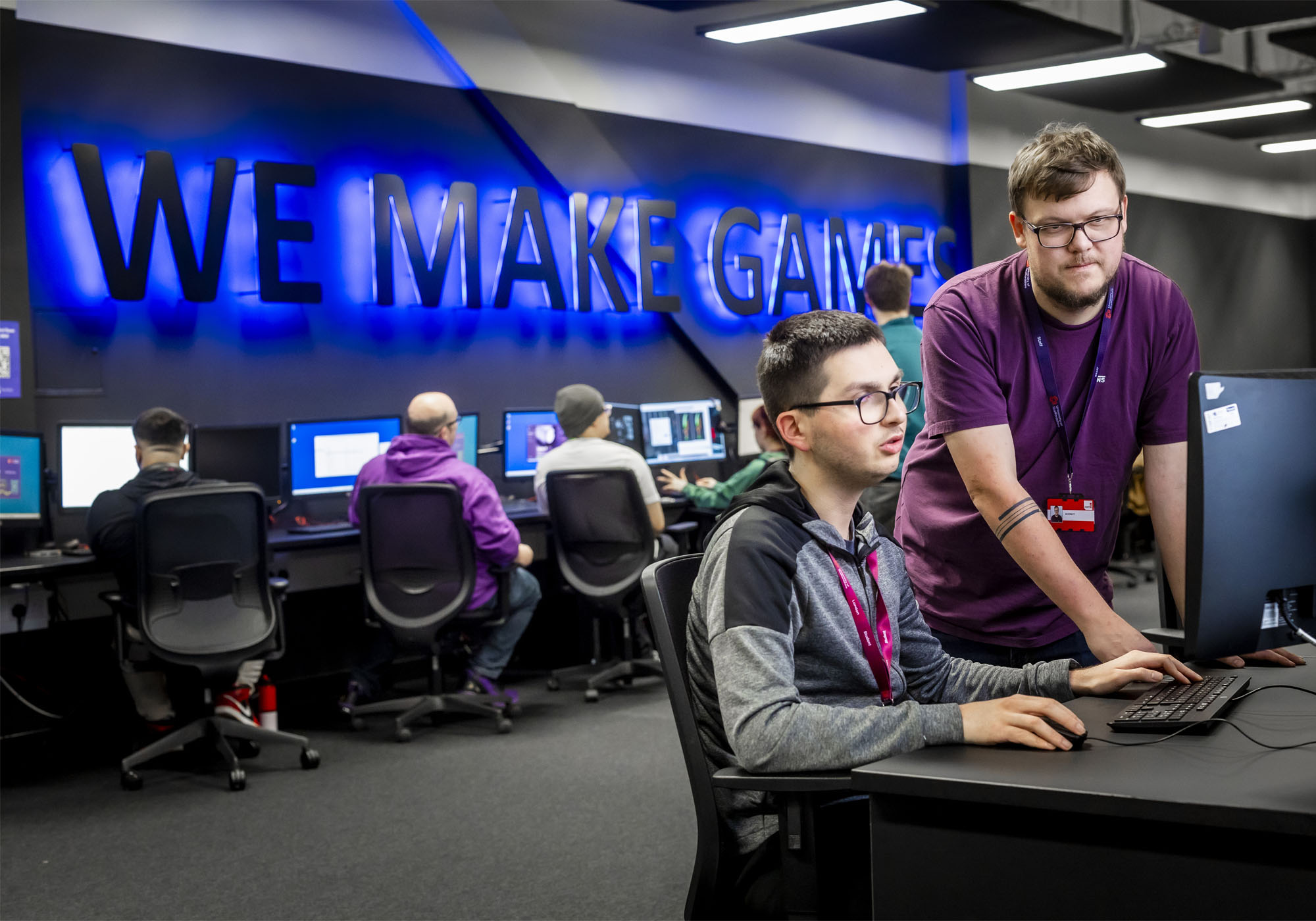 A male academic is helping a male student at his PC desk