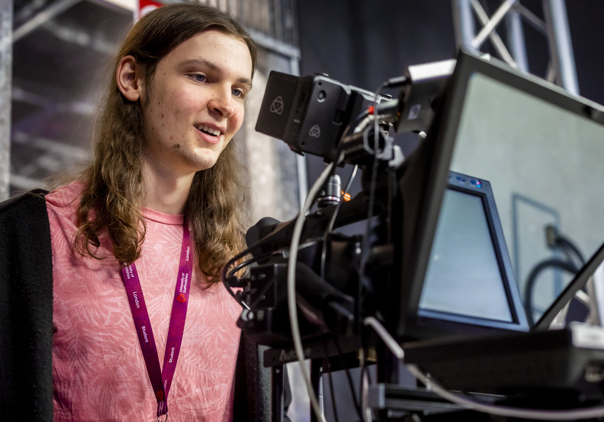 A young male student wearing a pink tshirt is using the recording equipment