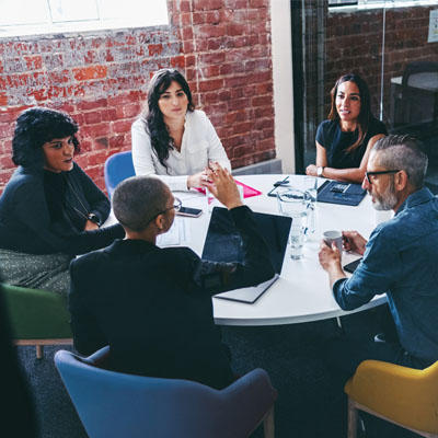 A mixed group of adults dressed in smart casual clothing are sitting and talking in an office with glass windows