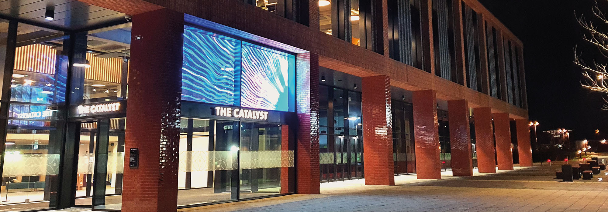 Outside the front entrance of the Catalyst building which is lit up at night time