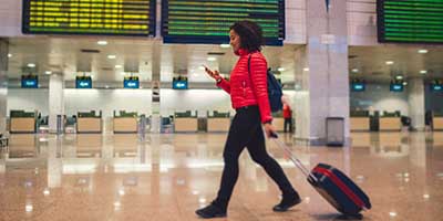 young mixed race female walks through a departure lounge at an airport pulling a small suitcase