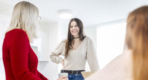 Three female students are in the kitchen chatting in light modern accommodation