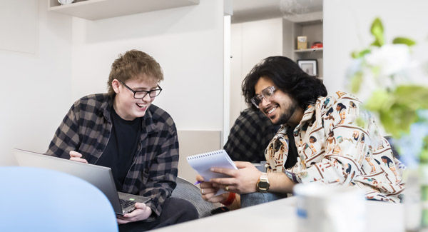 Two young males dressed casually are chatting and smiling with a laptop in a modern studio room