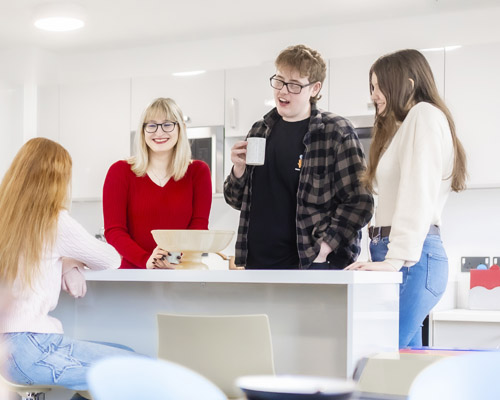 A group of young students are smiling and socialising in a modern kitchen with white decor