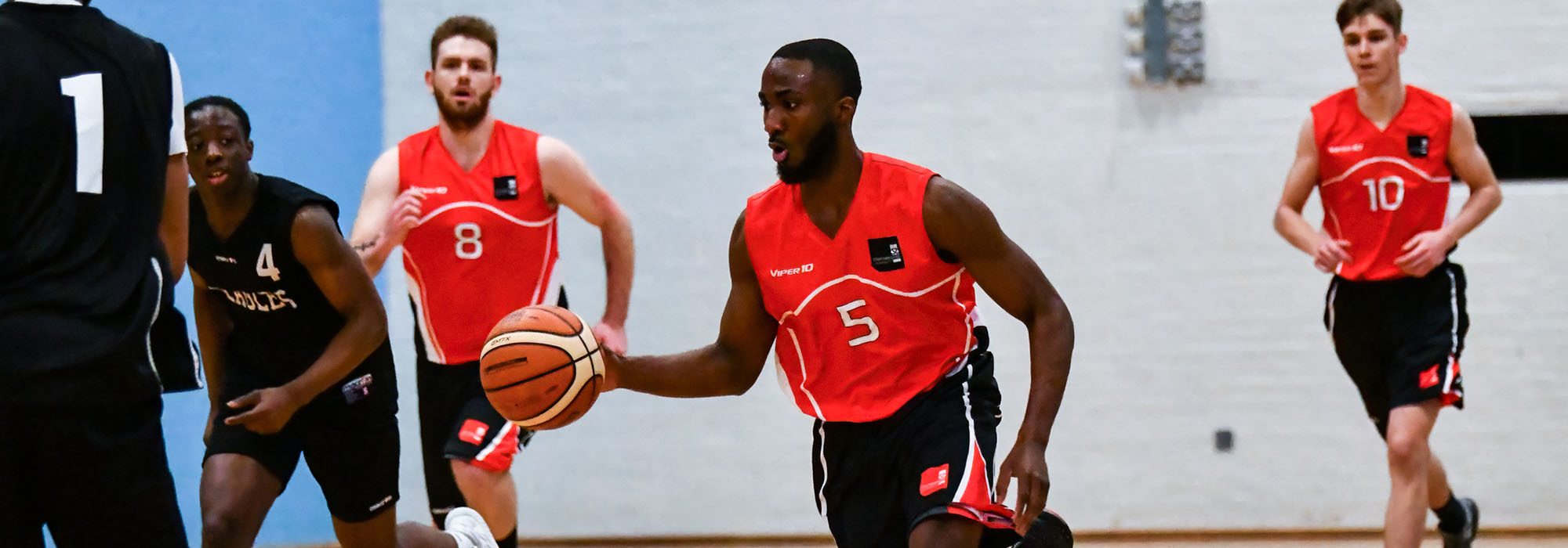 male basketball player dribbling across the court. His team mates are running behind him. They all wear red Staffs team basketball jerseys.