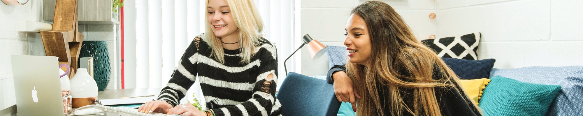 Two smiling female students using a laptop in their student accomodation