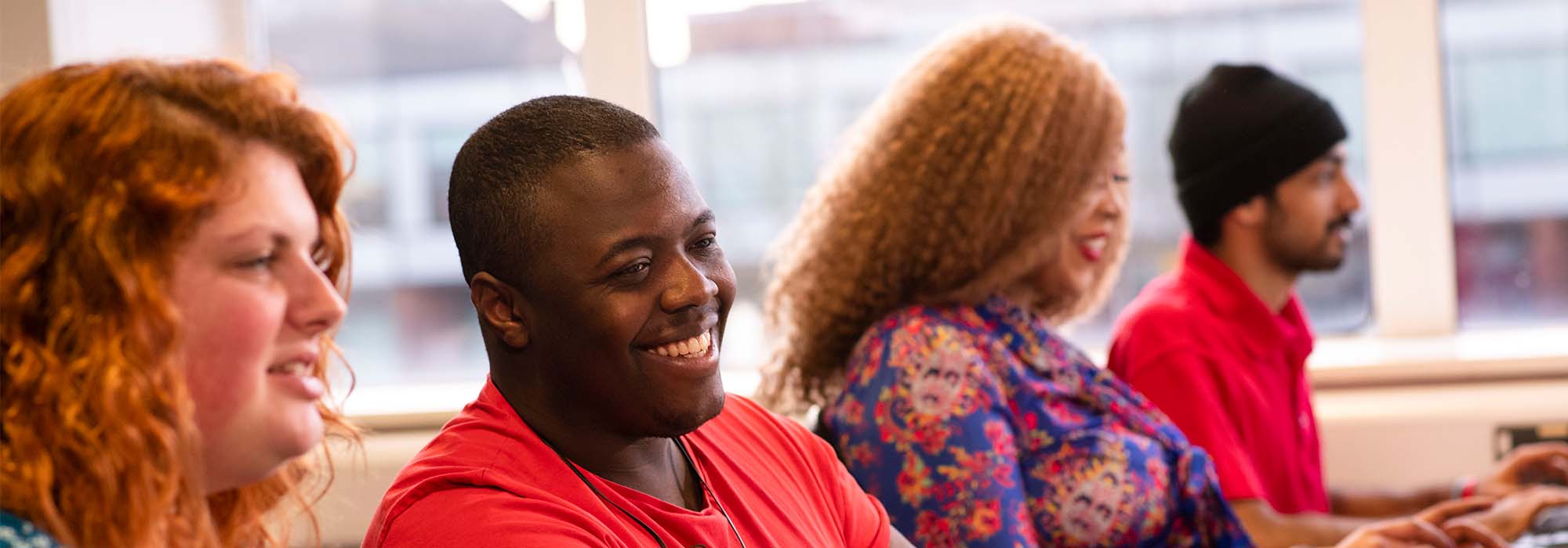 Male and female students working in computer lab. They are wearing brightly coloured clothing and are smiling.