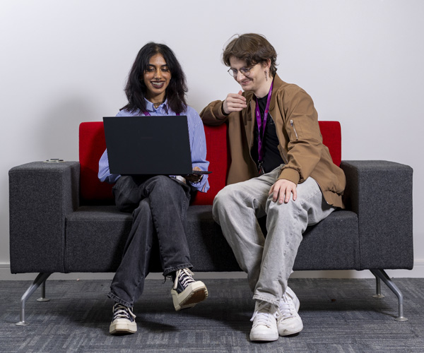 A young female with dark hair is using a laptop, she is sitting next to a young male student