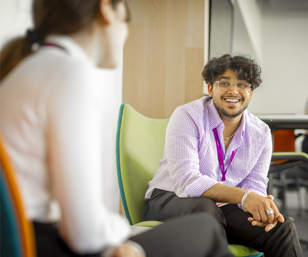 A smartly dressed male student is sitting in a modern office chatting to a female