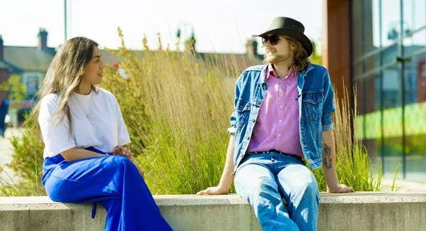 Two students dressed casually are sitting on a stone bench outside