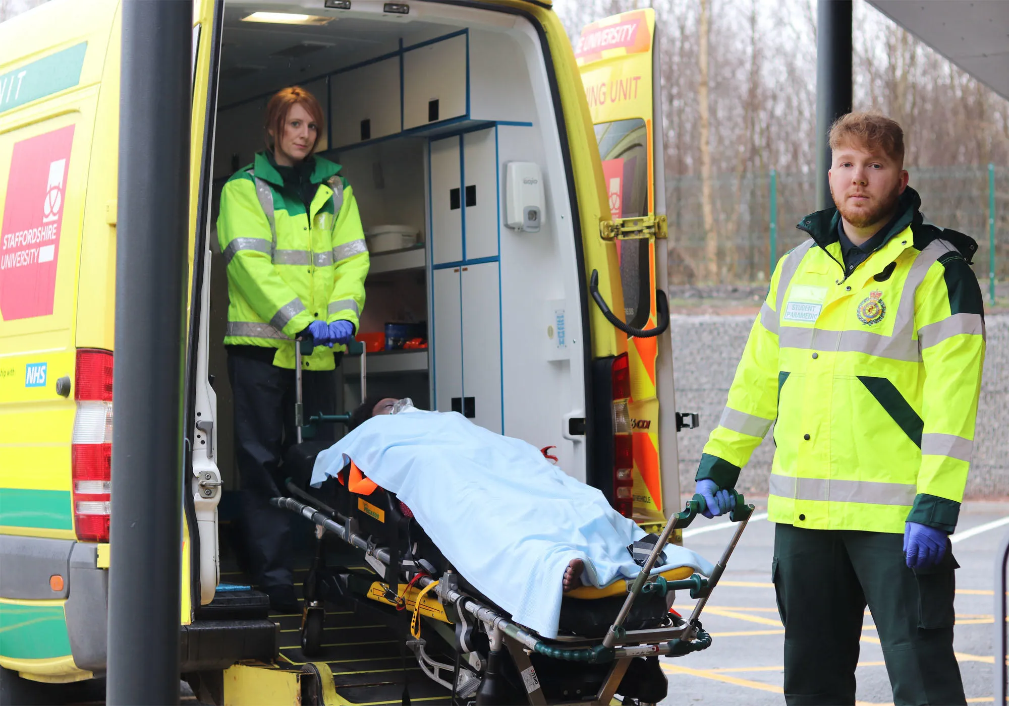 Paramedics students wearing uniform are wheeling out a patient