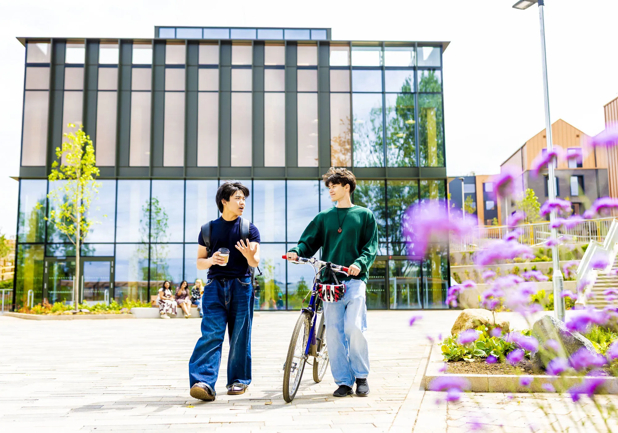 Students are walking outside the village hub chatting, one has a bicycle