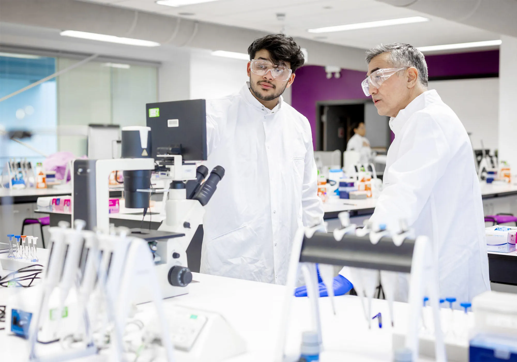 A student and lecturer are wearing white lab coats in the biomedical room