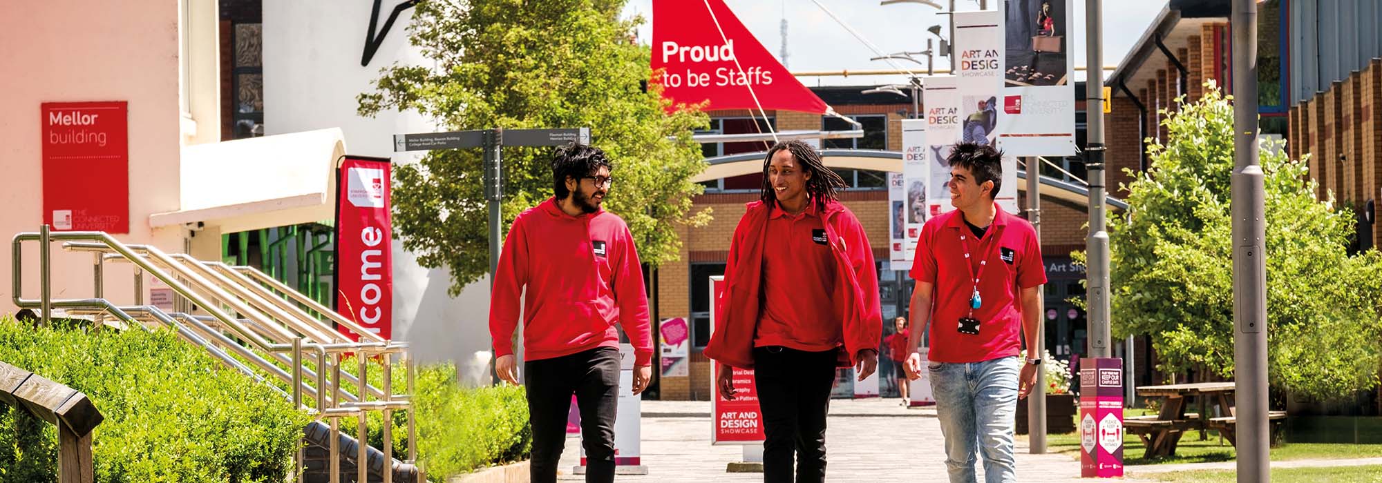 three student ambassadors walking through the college road campus, they are wearing red Staffordshire University jackets.
