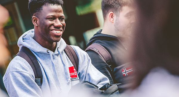 Male undergraduate student wearing a Staffordshire University hoodie smiles at friends