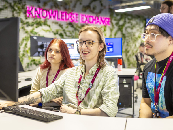 Three casually dressed students are collaborating on a PC in the knowledge exchange open space