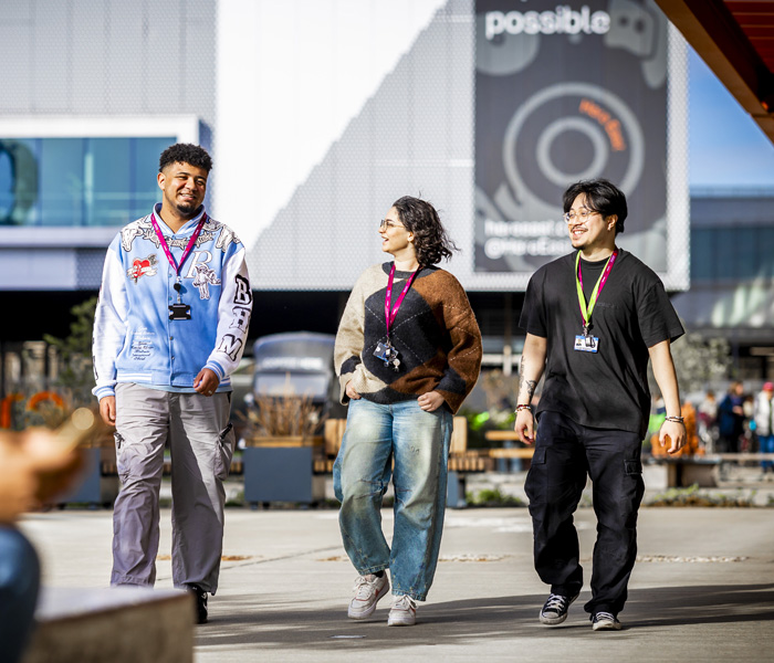 Three casually dressed students are chatting and walking outside the Here East campus in London