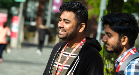 Two male students chatting, they are both wearing red Staffordshire University lanyards