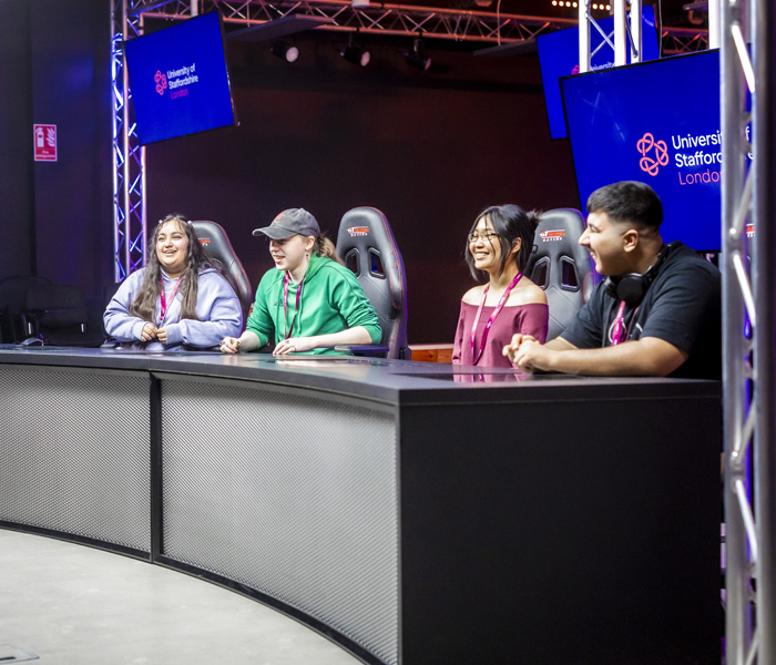 Casually dressed students are in the games streaming studio chatting at a desk