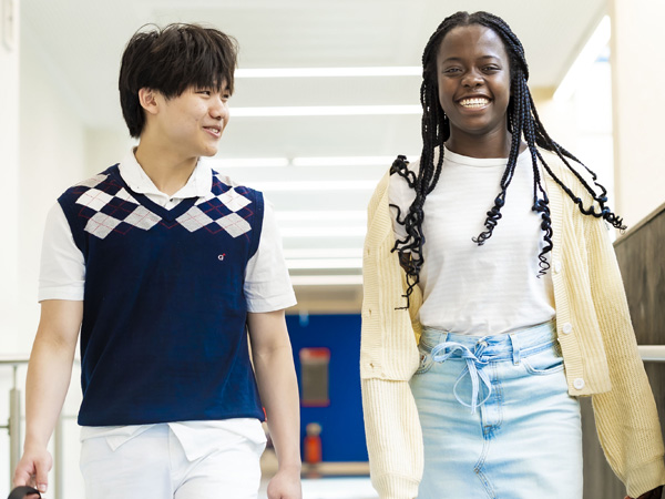A male and female student casually dressed, are smiling and in the corridor on campus