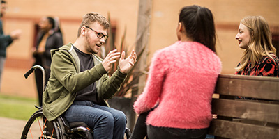 Male wheelchair user chats to two female students outside our accommodation at Stoke-on-Trent